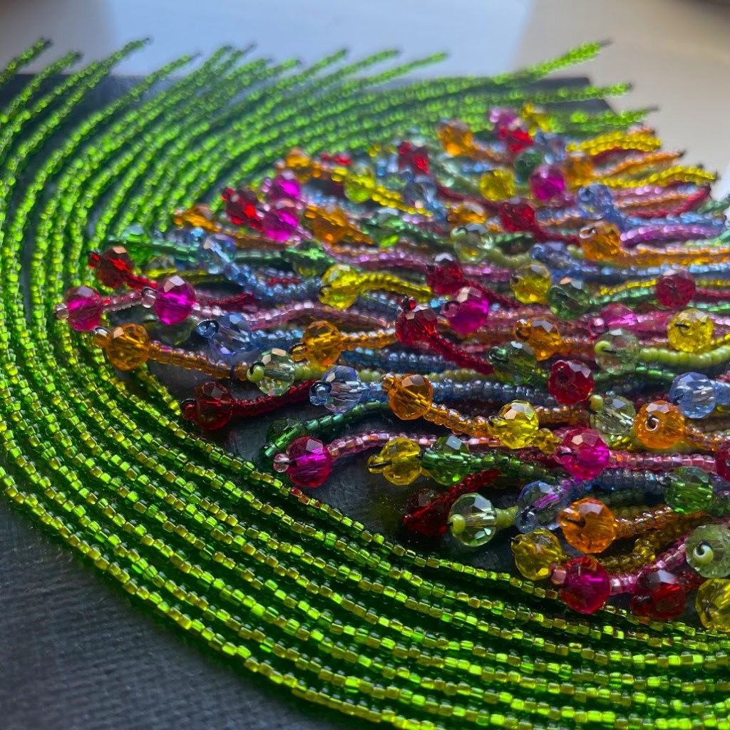 A colorful arrangement of beads with vibrant greens, pinks, yellows, and blues, creating an intricate design on a dark background.