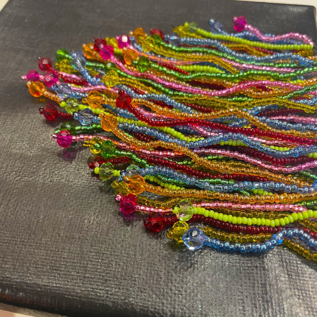 A colorful assortment of beaded strings, featuring various hues like pink, green, blue, and orange, arranged neatly on a black textured surface.